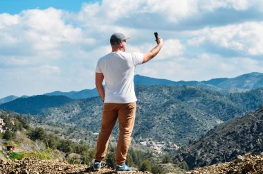 Adam cep telefonu kamerası ile selfie fotoğraf yapma hiking. Teknoloji ve seyahat kavramı. Uçurum yaz dağlarda üstünde duran genç adam.
