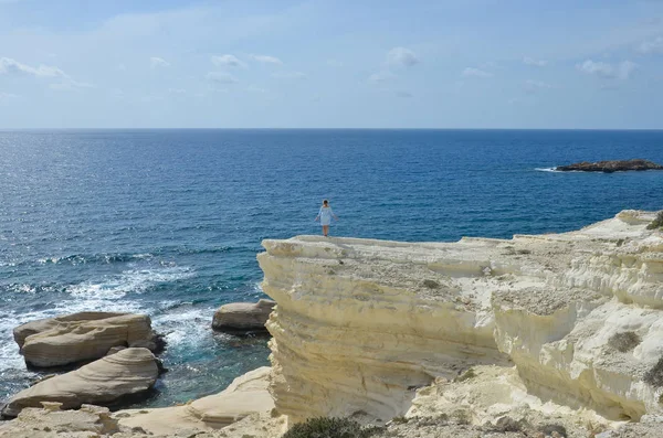 Woman near sea  standing on a cliff and look at the waves. Girl in blue dress. Wanderlust travel concept. Sea vacation concept. Freedom and travel concept. Mediterranean Sea