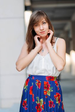 Kadın yüzünü elleri ile dokunarak. Sokak, kentsel arka plan üzerinde genç güzel kadın. Kadın portre açık havada çiçek etek ve beyaz bluz.