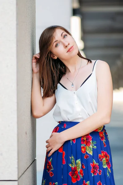 Woman in floral skirt and white top outdoors. Young beautiful woman on the street, urban background. Half-length portrait, woman in stylish clothes, lifestyl