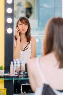 Makyaj aynası ampul ışıkları ile seyir ve yüzünü dokunaklı genç çekici kadın. 