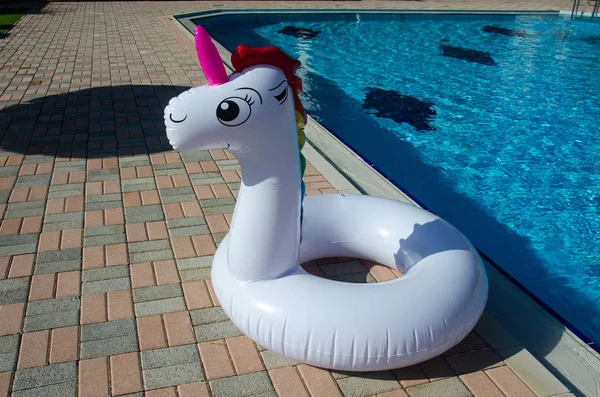 Unicorn swim tube near pool. Unicorn inflatable float for kids and adult. Summer holidays, beach vacation. Fantasy swim ring.