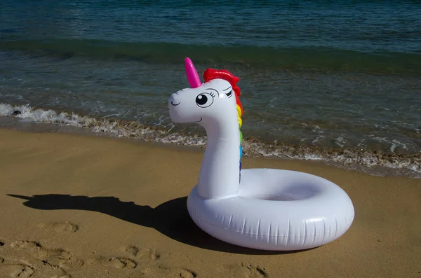 Unicorn pool ring, unicorn pool float on sand near sea. Inflatable unicorn. Summer holidays, beach vacation.