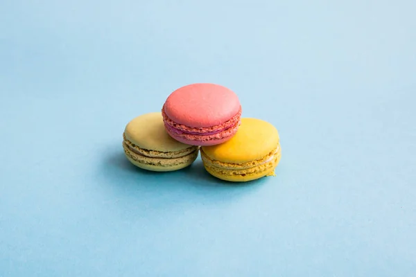 Colorful macaroons, pink, yellow and green macaroons on blue background. Sweets, desserts. Copyplace, place for text.