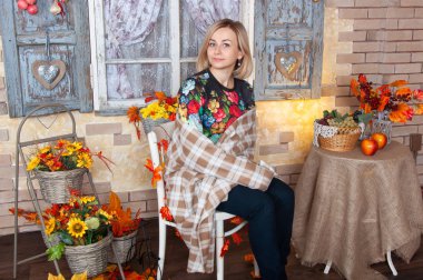 Sonbahar kadını dekore edilmiş evde oturmuş bir battaniyeye sarılmış. Arka planda, sonbahar natürmort düşmek. 