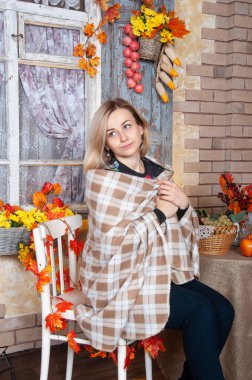 Sonbahar kadını dekore edilmiş evde oturmuş bir battaniyeye sarılmış. Arka planda, sonbahar natürmort düşmek. Sıcak milattan genç güzel kadın