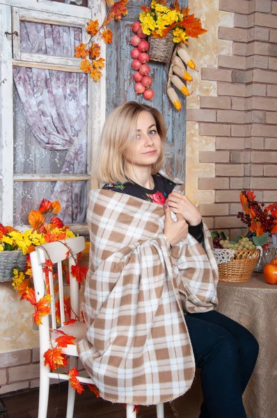 Happy woman enjoying the autumn. Autumn woman wrapped in a blanket sitting at decorated home. Autumn still life on background, fall.