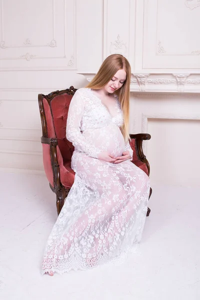 坐在扶手椅在家和看她的肚子的孕妇 — 图库照片