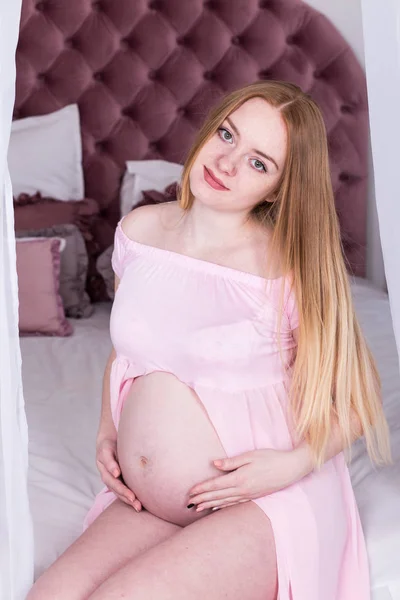 怀孕的妇女坐在床上抚摸她的肚子 人和期望概念 — 图库照片