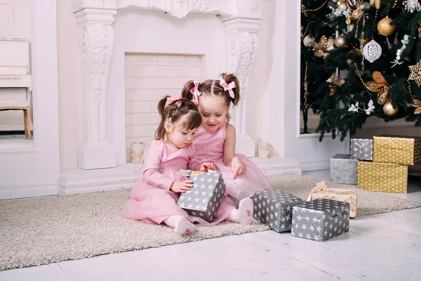 带着圣诞礼物的女孩两个孩子有乐趣与圣诞树 图库图片