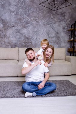 Aile evde piliçle oynuyor ve gülümsüyor. Anne, baba ve kız gülümsüyor ve oynuyorlar.