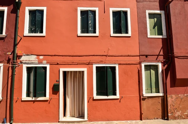 Windows with green shutters in Mediterranean style on orange wall. Colourful painted windows. Burano island near Venice, Italy. Abstract background, texture