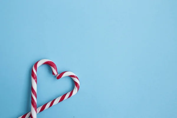 Heart made of candy canes isolated on blue background. Candy canes arranged in a heart shape. Love concept. Copyplace, space for text and logo.