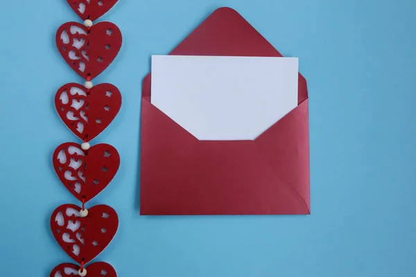 Open red envelope with blank white and gift card and red hearts decoration. on blue background. Valentines day background with hearts. Copyplace, space for text and logo.