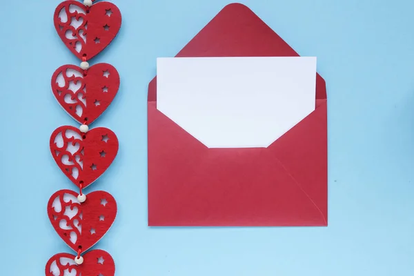 Red envelope with white gift card and hearts decoration on blue background. Copyplace, space for text and logo.