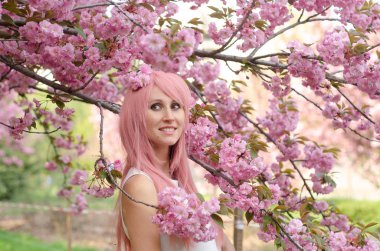 Sakura çiçekli ağacın yanındaki kadın. Çiçek açan pembe saçlı kız.