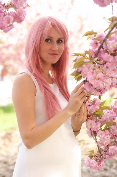 Sorrindo mulher grávida tocando sakura rosa árvore florescendo — Fotografia de Stock