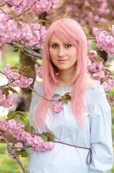 Mulher sorridente com cabelo rosa perto de flores sakura. Mulher grávida — Fotografia de Stock