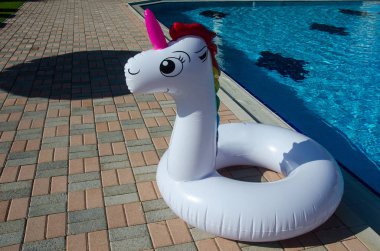 Şişme tek boynuzlu at mavi su ile havuz yakınında yüzer. Yaz holi