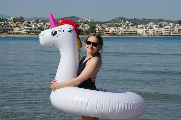 Mujer abrazando unicornio inflable cerca del mar con Chania Creta espalda — Foto de Stock