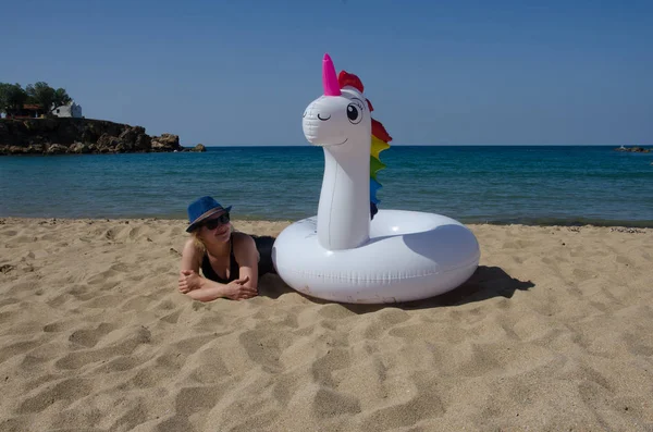 Mujer relajante en la playa con flotador de piscina de unicornio inflable cerca — Foto de Stock