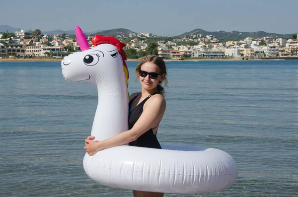 Mujer con unicornio inflable cerca del mar. Joven mujer de moda stan — Foto de Stock