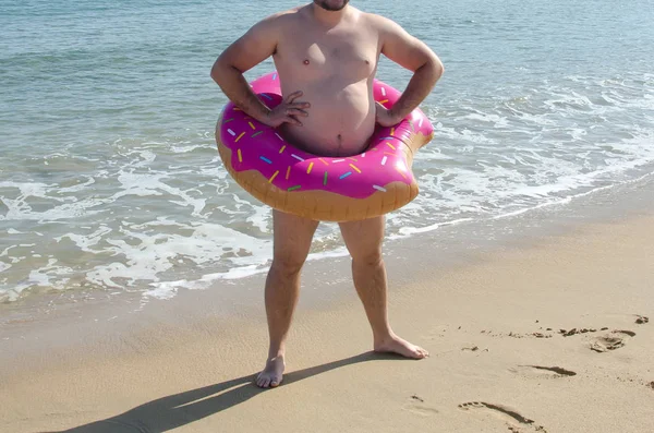 Hombre obeso vistiendo anillo inflable de rosquilla en su vientre en la playa. C — Foto de Stock