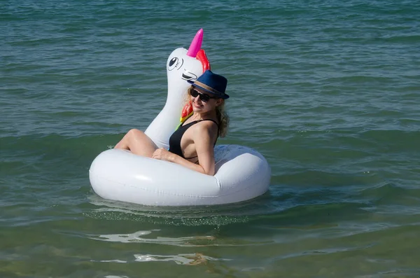 Mujer sonriente flotando en la piscina de unicornio inflable flotar en el mar — Foto de Stock