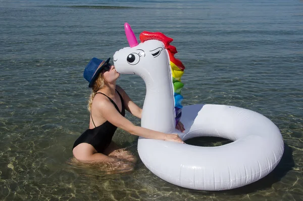 Woman kissing inflatable unicorn pool float on sea on beach. Sum