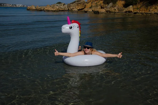 Mujer mostrando pulgares hacia arriba relajándose con unicornio inflable en el mar — Foto de Stock