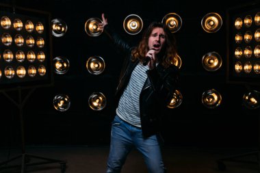 erkek şarkıcı parlak fenerler, çerçevede uzun saçlı sahne alanı üzerinde mikrofon ile sahne