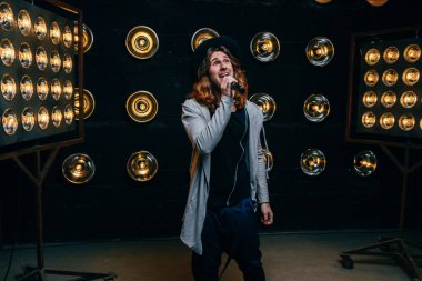 erkek şarkıcı parlak fenerler, çerçevede uzun saçlı sahne alanı üzerinde mikrofon ile sahne