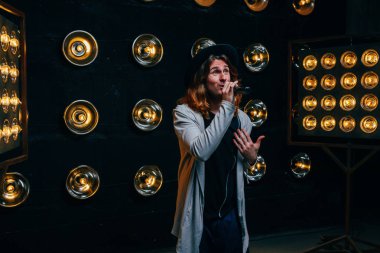 erkek şarkıcı parlak fenerler, çerçevede uzun saçlı sahne alanı üzerinde mikrofon ile sahne