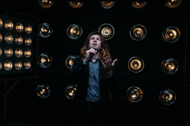 Parlak fenerler, çerçevede uzun saçlı sahne alanı üzerinde mikrofon ile acımasız şarkıcı sahne