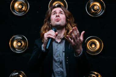 Parlak fenerler, çerçevede uzun saçlı sahne alanı üzerinde mikrofon ile acımasız şarkıcı sahne