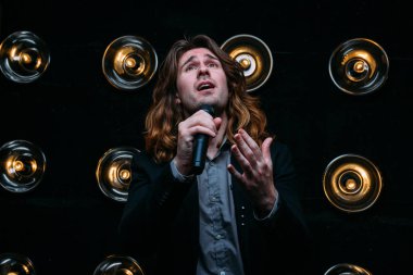 Parlak fenerler, çerçevede uzun saçlı sahne alanı üzerinde mikrofon ile acımasız şarkıcı sahne