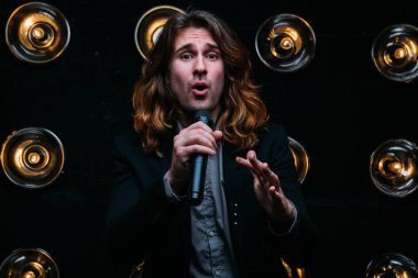 Parlak fenerler, çerçevede uzun saçlı sahne alanı üzerinde mikrofon ile acımasız şarkıcı sahne