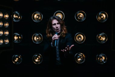 Parlak fenerler, çerçevede uzun saçlı sahne alanı üzerinde mikrofon ile acımasız şarkıcı sahne