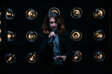 Parlak fenerler, çerçevede uzun saçlı sahne alanı üzerinde mikrofon ile acımasız şarkıcı sahne