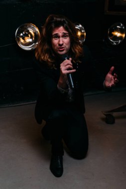 Parlak fenerler, çerçevede uzun saçlı sahne alanı üzerinde mikrofon ile acımasız şarkıcı sahne