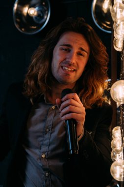 Parlak fenerler, çerçevede uzun saçlı sahne alanı üzerinde mikrofon ile acımasız şarkıcı sahne