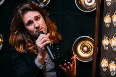 Parlak fenerler, çerçevede uzun saçlı sahne alanı üzerinde mikrofon ile acımasız şarkıcı sahne