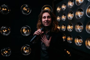 Parlak fenerler, çerçevede uzun saçlı sahne alanı üzerinde mikrofon ile acımasız şarkıcı sahne