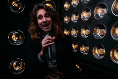 Parlak fenerler, çerçevede uzun saçlı sahne alanı üzerinde mikrofon ile acımasız şarkıcı sahne