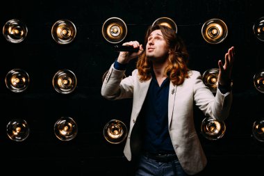 erkek şarkıcı parlak fenerler, çerçevede uzun saçlı sahne alanı üzerinde mikrofon ile sahne