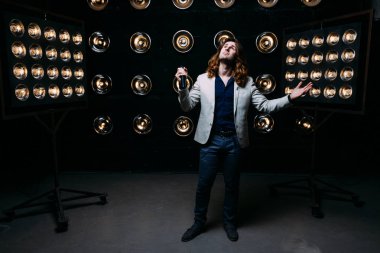 erkek şarkıcı parlak fenerler, çerçevede uzun saçlı sahne alanı üzerinde mikrofon ile sahne