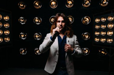 erkek şarkıcı parlak fenerler, çerçevede uzun saçlı sahne alanı üzerinde mikrofon ile sahne