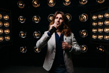 erkek şarkıcı parlak fenerler, çerçevede uzun saçlı sahne alanı üzerinde mikrofon ile sahne