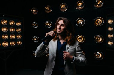 erkek şarkıcı parlak fenerler, çerçevede uzun saçlı sahne alanı üzerinde mikrofon ile sahne