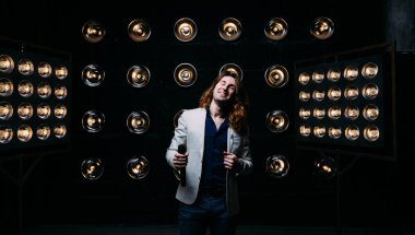 erkek şarkıcı parlak fenerler, çerçevede uzun saçlı sahne alanı üzerinde mikrofon ile sahne